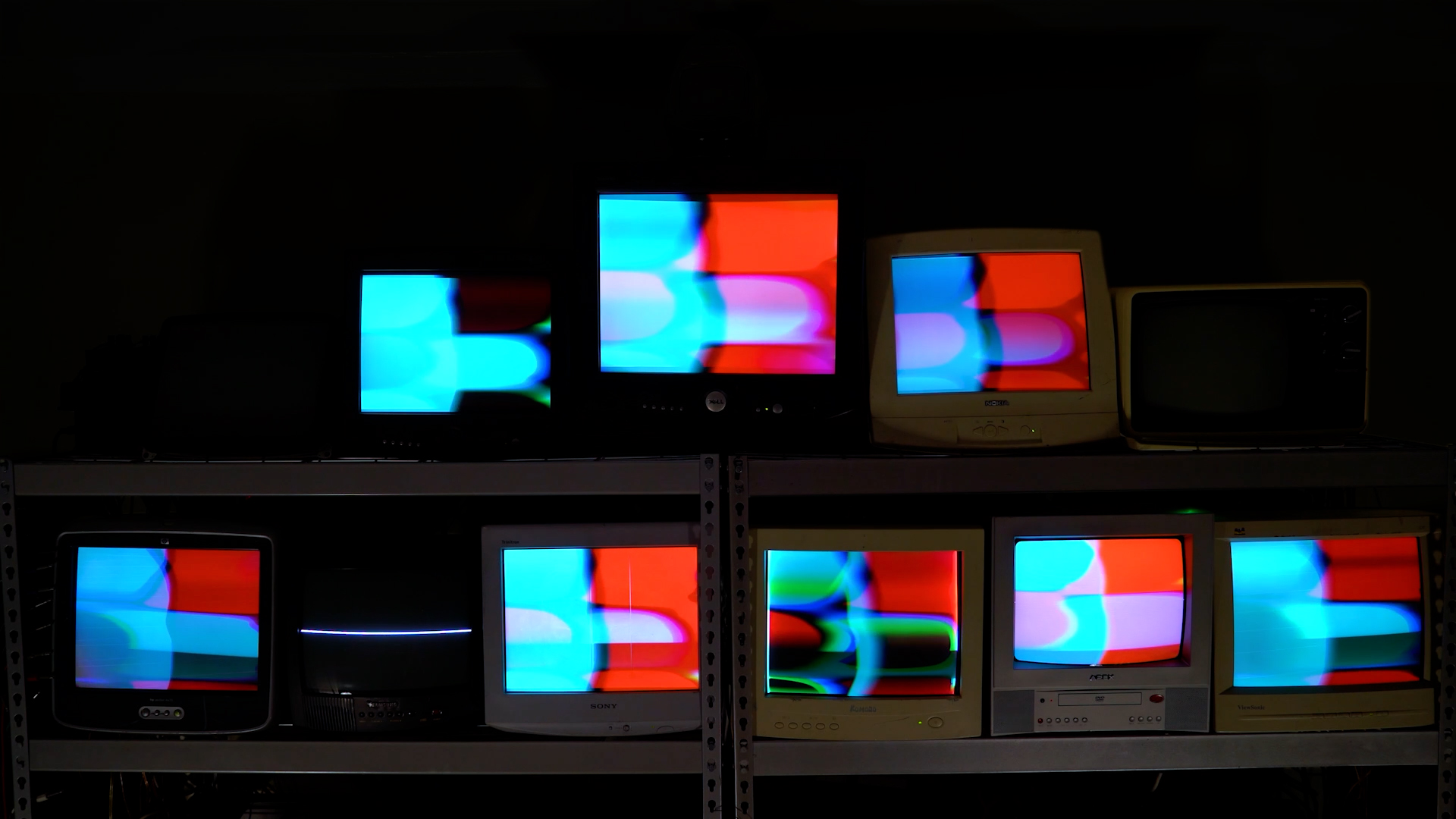Closeup of 8 CRT monitors showing bright video synthesis, one broken CRT monitor showing a horizontal line, and two CRT monitors turned off with a dark background.