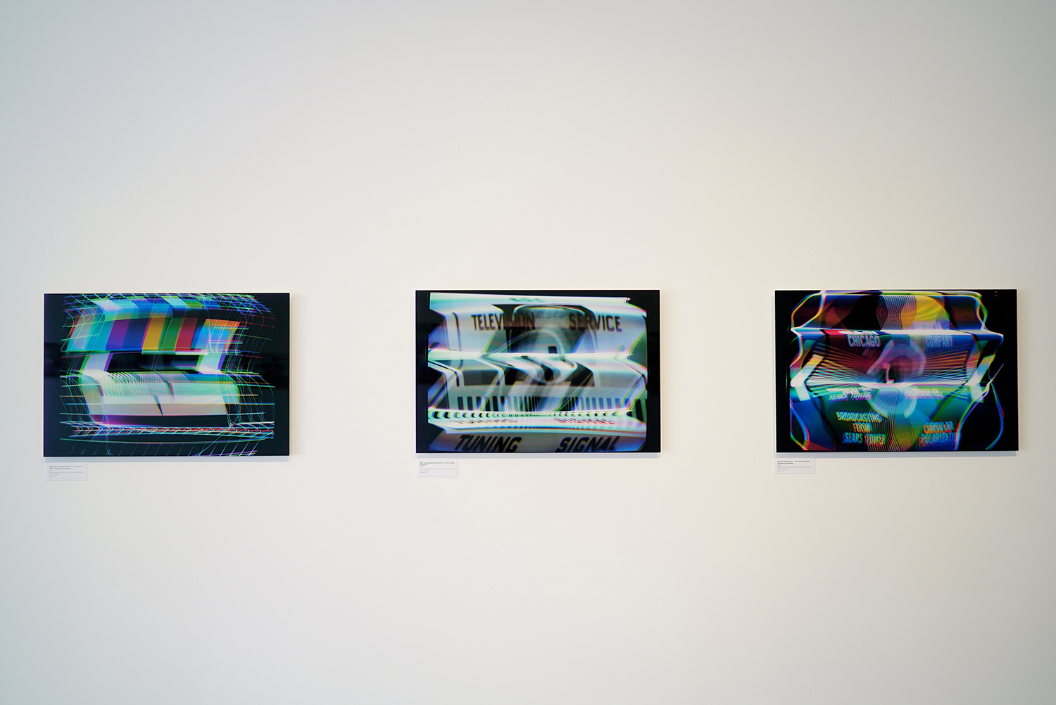 Face-mouted prints hanging on wall photographed at a sharp angle with a shallow depth of field.