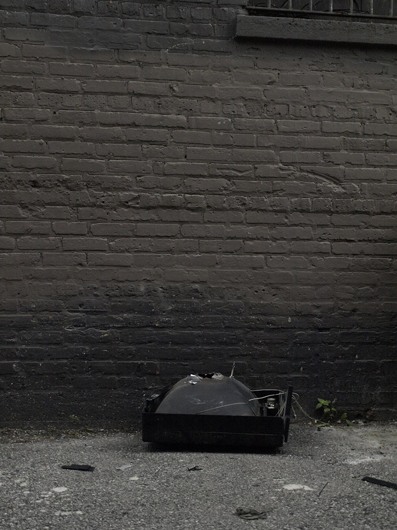 A cathode ray tube television broken and face down in an alley with the plastic case missing.