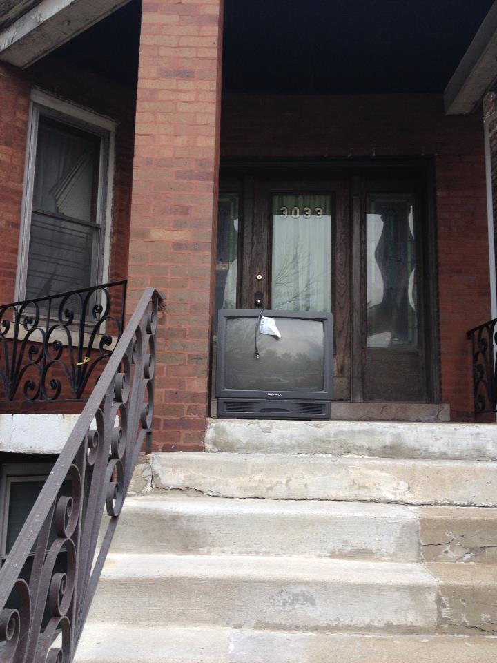 A CRT television on the porch of a brick building..