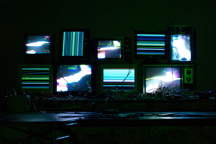 9 CRT televisions and computer monitors with bright glitchy imagery.
