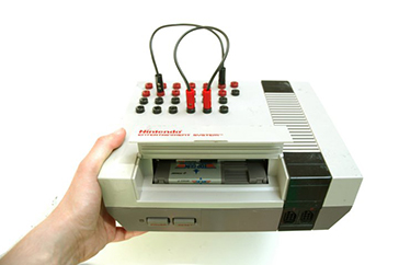 A modified Nintendo Entertainment System console held by a hand with patch cables going into the top.